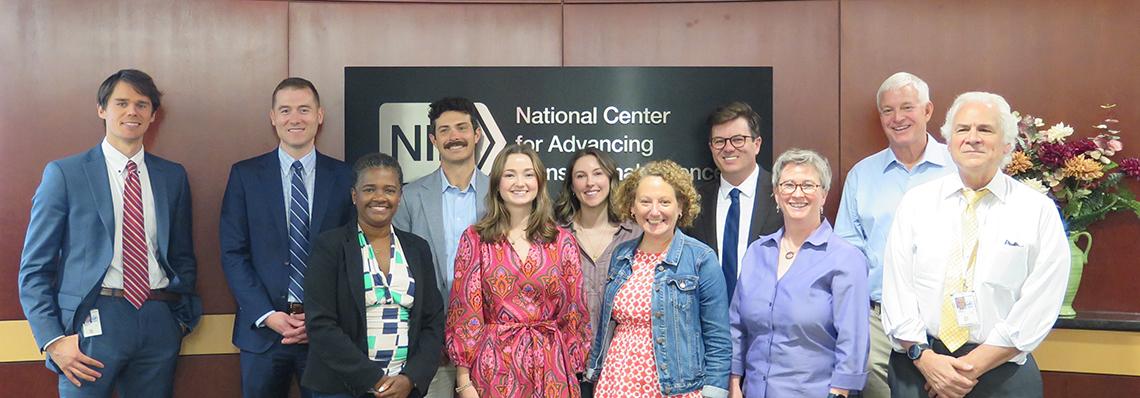 A large group stands together smiling in front of NCATS sign on wall.