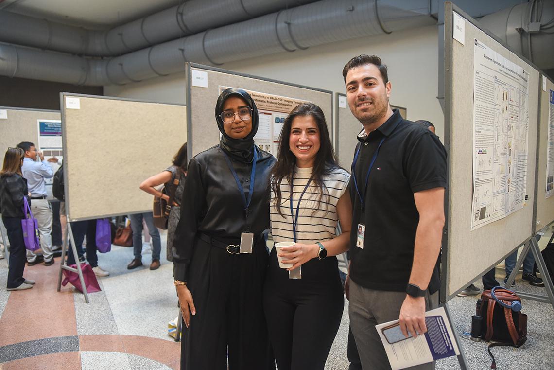 Three colleagues stand in front of a poster