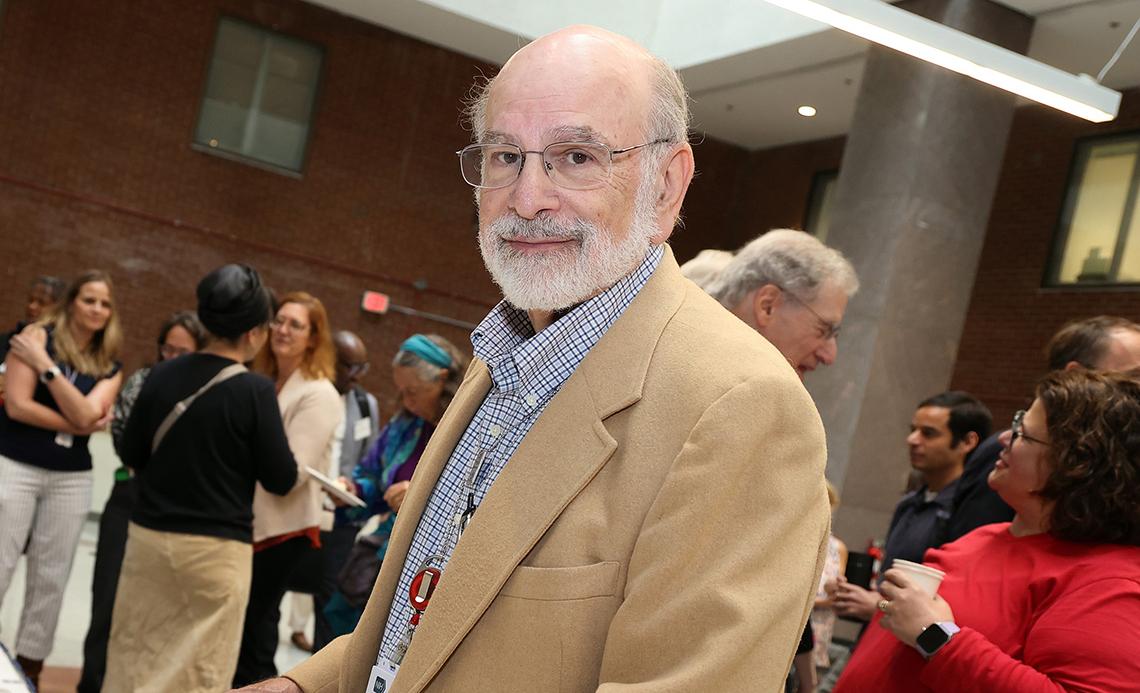 A smiling Dr. Goldstein stands in a large room filled with his colleagues.