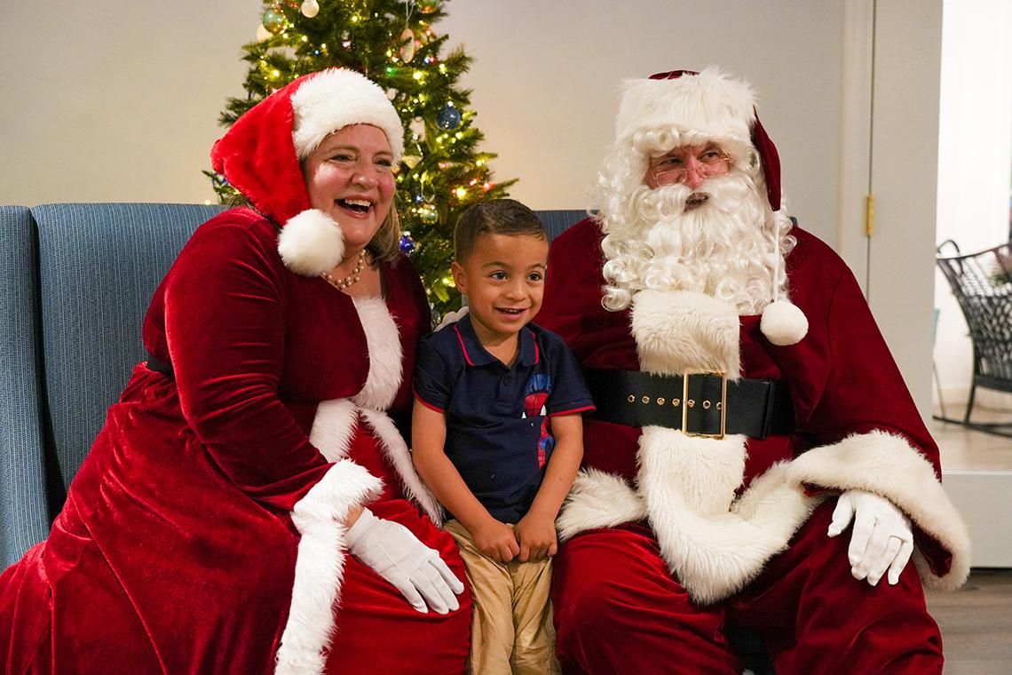Santa Claus, Mrs. Claus and a young friend smile at a person out of the right frame.