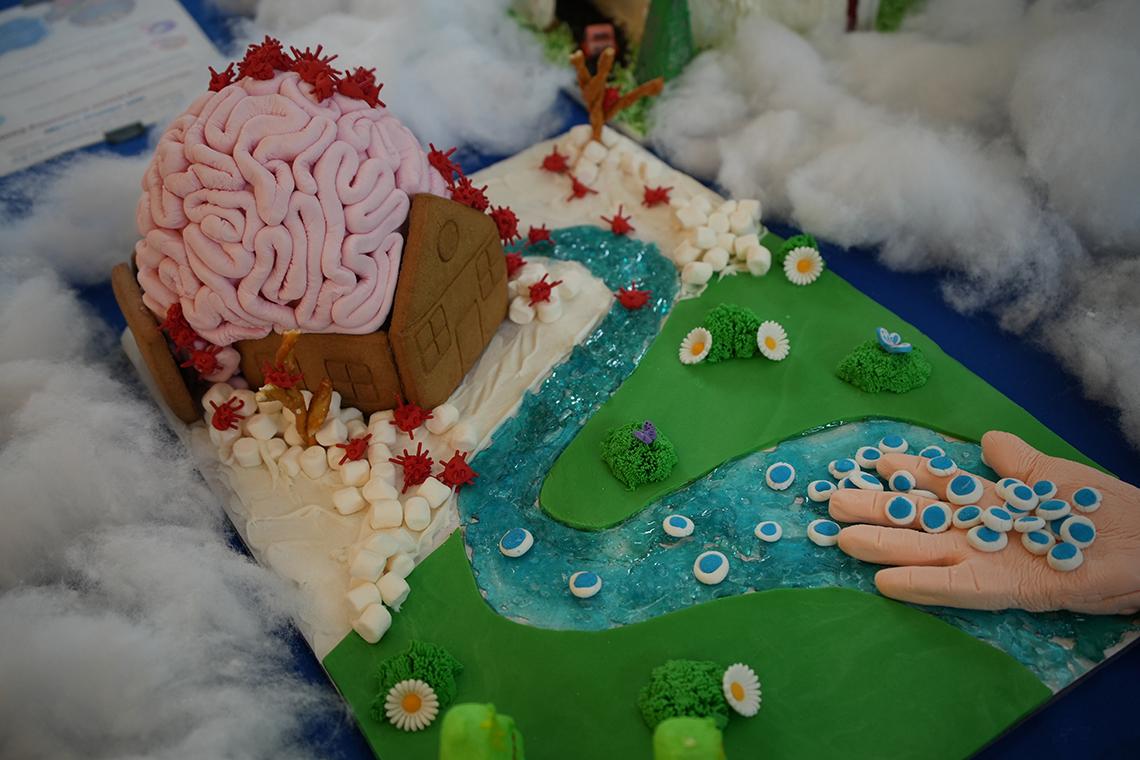 A hand holds candy cells that lead to a gingerbread house with a brain for a roof